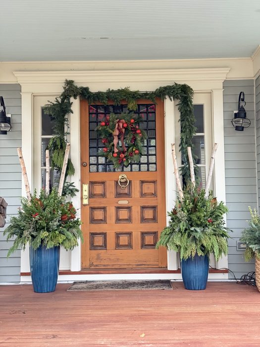 Front entrance with paired blue urns, birch branches, and evergreen greens flanking a garland and wreath on the door